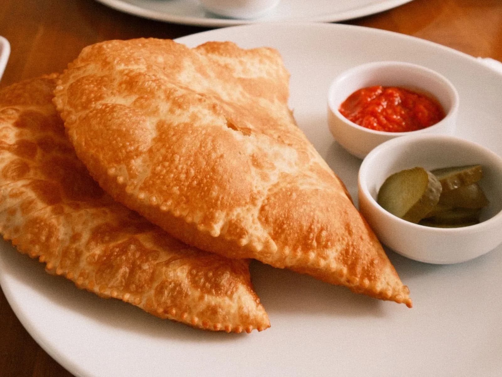 Twee gefrituurde çibörek op een bord, met augurken en pikante saus
